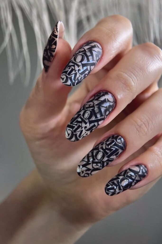 Nude almond nails featuring intricate black lace-inspired nail art.