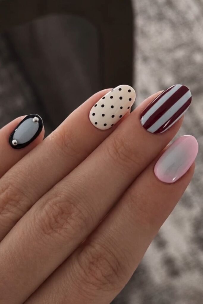 Almond nails featuring burgundy stripes, black accents, white polish and tiny polka dots.